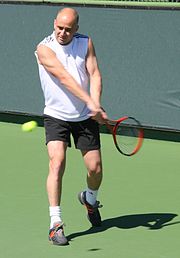 A man wearing white clothing looking at a tennis racket