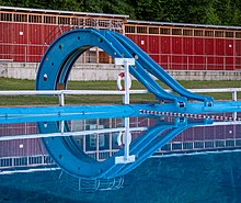 Two blue body slides, similar to playground slides, on the far side of a swimming pool