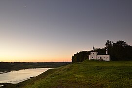 Photographie d'une église sur une colline dominant un lac à la tombée de la nuit.