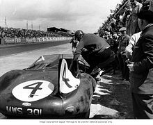 A driver (Sanderson or Flockhart) entering the winning Jaguar D-Type during a pit stop.
