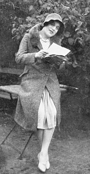 Full body photograph of Lili Elbe. She is looking at the camera while holding a letter