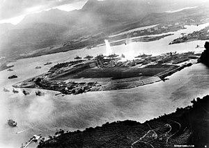 Foto fra et japansk fly af Battleship Row i begyndelsen af angrebet. Eksplosionen i midten er en torpedo der rammer USS Oklahoma. To angribende japanske fly kan ses: én over USS Neosho og én over flåde værftet.