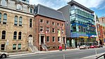 Exterior facade of buildings on the north side of Adelaide Street. Two 19th century brick buildings to the left/west next to a 21st-century glass building.