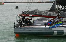 Arrière du bateau gris qui navigue dans un grand port de commerce. Plusieurs hommes dans le cockpit. Le barreur salue le photographe.