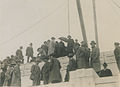 An old photo of a lot of men in suits and trenchcoats standing on top of the stone structure of the Cardston Alberta temple. Poles and wires are seen from the top.