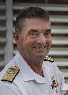 Colour photo of a man wearing a white uniform standing behind a lectern