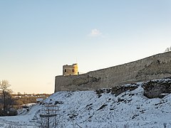 Photographie d'une tour médiévale d'une forteresse médiévale sur un promontoire rocheux dominant une vallée enneigée.