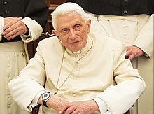Benedict seated in a white cassock and gold pectoral cross