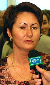 A woman with brown hair, speaking into a microphone.