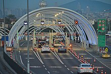 Two two lane roads depicted. At the bottom left, a car is travelling. At the bottom right, a van parked on diagonally-crossed marked no-entry section. Two lane road on the right splits into a tunnel and a single-lane exit.