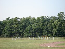 Green field with green trees in the background. Large, wooden letters in the foreground spell "C A M P W E S T M O N T."