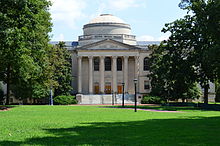 A large building with six Corinthian columns on the front with the sides being obscured by bushes.