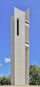 A tall modern concrete structure of three slabs, with the bells ensconced in the middle at the top, surrounded by landscaped grass and hedge.