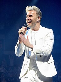 A waist-up shot of Gary Barlow, singing into a microphone.