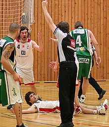 Arbitre signalant une faute en levant le bras. Le joueur fautif est couché sur le parquet