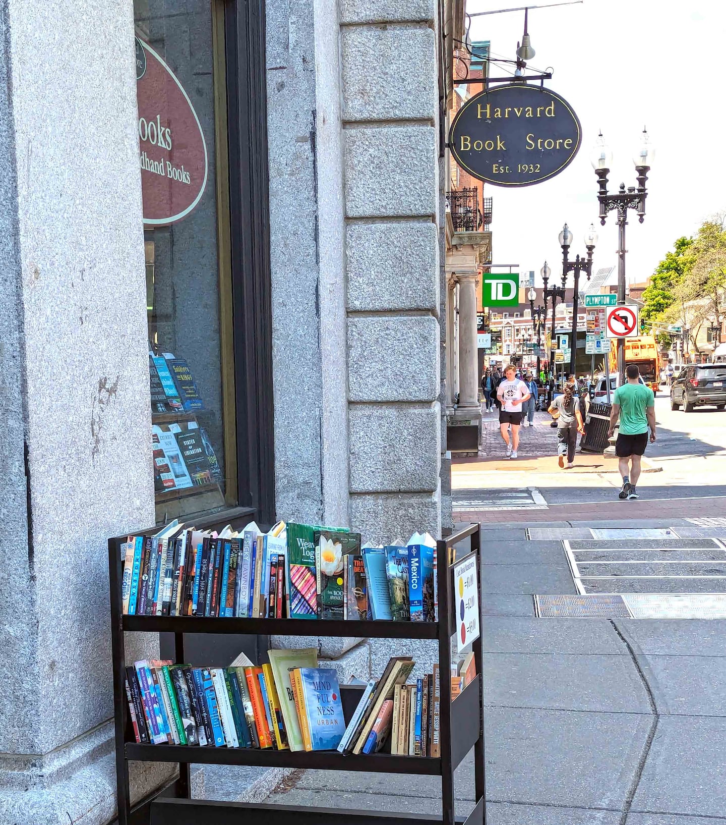 A cart of bargain books on the sidewalk helps to lure bibliophiles into Harvard Book Store.