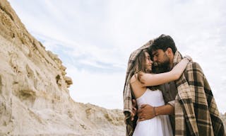 Beautiful couple of lovers hugging under blanket in sand canyon with cloudy sky — Photo by IuliiaVerstaBO