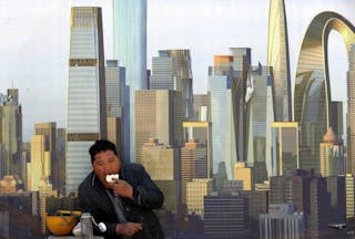 A construction worker eats a bun during a lunch break in front of a wall of a construction site in Beijing