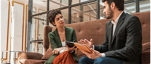 Two persons sitting, holding tablets and discussing on some topic.