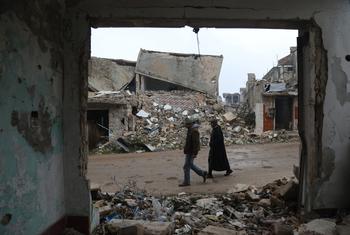 两个人走过被炸毁的叙利亚西部巴拉村的废墟。