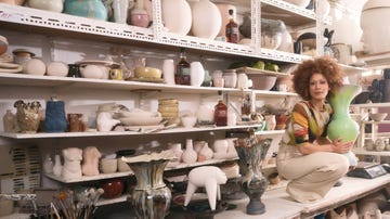 a person sitting in a room with shelves full of vases and pottery