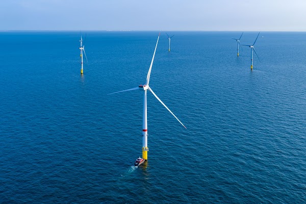 Six offshore windmills sit in the ocean against a blue sky