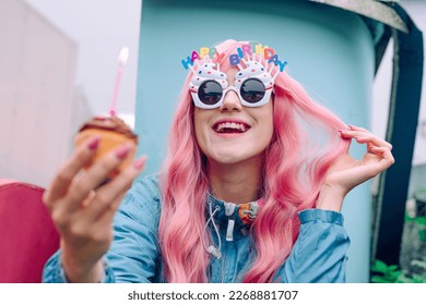 誕生日を祝うカップケーキを持つ目新しい眼鏡をかけた幸せな女性の写真素材