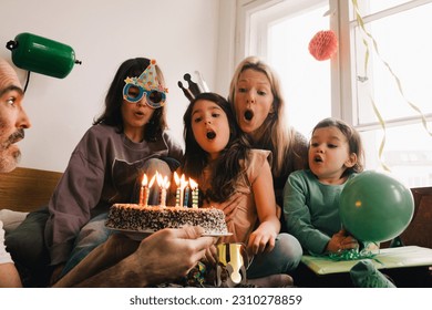 Man holding birthday cake with burning candles in front of surprised family at home Stock Photo