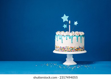 White birthday drip cake with teal ganache, star toppers and fun candles over dark blue background Stock Photo