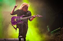 Image d'un homme blond jouant sur scène avec une guitare électrique violette