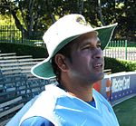 The head and shoulders of a man in his 30s, wearing a white and green wide-brimmed hat, and a blue top.