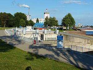 Bremer Weserkraftwerk von Westen, links beim Zaun Gitterstreifen über dem Fischpass, im Hintergrund das Wärmekraftwerk Hastedt