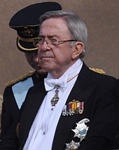 Photographie d'un homme aux cheveux blancs vêtu d'un costume.