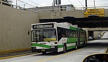 Green-and-white articulated bus leaving an underpass