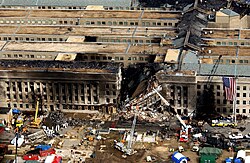 Aerial view showing damaged, burned, and collapsed portion of the Pentagon with firefighting and rescue equipment nearby