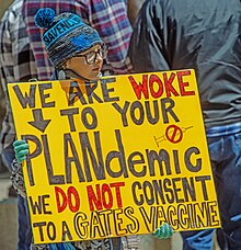 A young adolescent carrying a yellow sign saying, "We are woke to your plandemic. We do not consent to a Gates Vaccine."