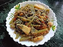 A white bowl containing 'Laau shaaker posto', which is a typical Bengali dish made with the stems and leaves of a bottle gourd plant, potatoes, and 'bori' which is sundried dollops of lentil paste. It's cooked in poppy seed-mustard paste.