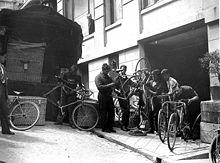 Some persons looking at and doing things to bicycles.