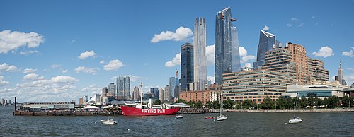 Au-dessus d'une étendue d'eau calme, des gratte-ciel et quelques blocs de bâtiments. Un quai s'avance dans l'eau, auprès duquel un bateau rouge est accosté. Quelques arbres bordent l'eau.