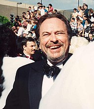 Rip Torn, a caucasian male in his early-60s with dark hair, wears a black suit and white shirt with a black bow-tie. He laughs and smiles.