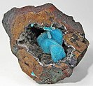 Dans une poche ouverte dans une matrice de limonite, amas de chrysocolle bleue recouverte de quartz drusique.