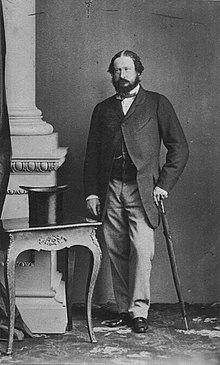 Black-and-white photo of a bearded Anglesey wearing a suit and waistcoat and holding a walking stick.