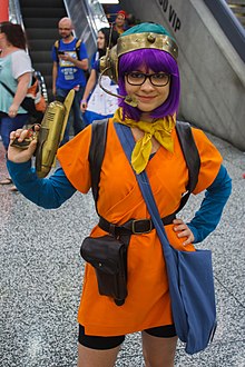 Femme souriante habillée en orange et portant des lunettes.