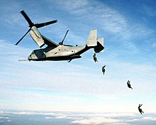 Four U.S. Marine paratroopers jump from the rear loading ramp of a MV-22 Osprey.