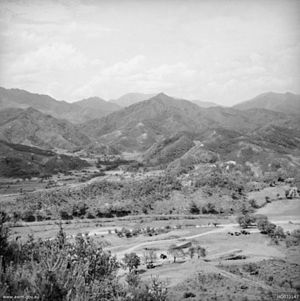 A series of ridgelines and steep hills in the distance, with light to medium vegetation. In the foreground is an open valley.