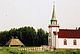 View of the side facade of Ste. Anne's Roman Catholic Church, with corner towers and projecting spire, and teepees