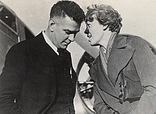 Photographie noir et blanc de Charles Ulm et Amelia Earhart discutant (Amelia lui parlant directement dans l'oreille).