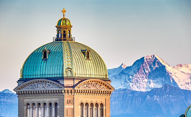 Federal Palace in Bern. Central dome crowned by the Swiss Cross in evening light with a perspective setting it close to the north face of the mountain Eiger.