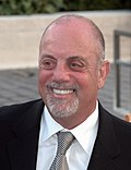 An upper body shot of a man wearing a shirt, suit and tie. He is balding and his smiling mouth is framed by a white goatee beard.