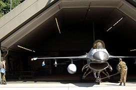 Un caza F-16 diante dun hangar protexido.